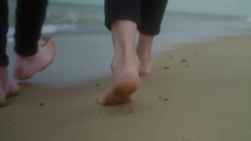Barefoot couple walking over the wet sand next to the ocean