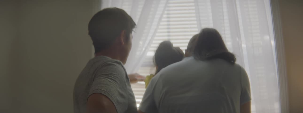 A family in a room looking out a window with curtains and blinds