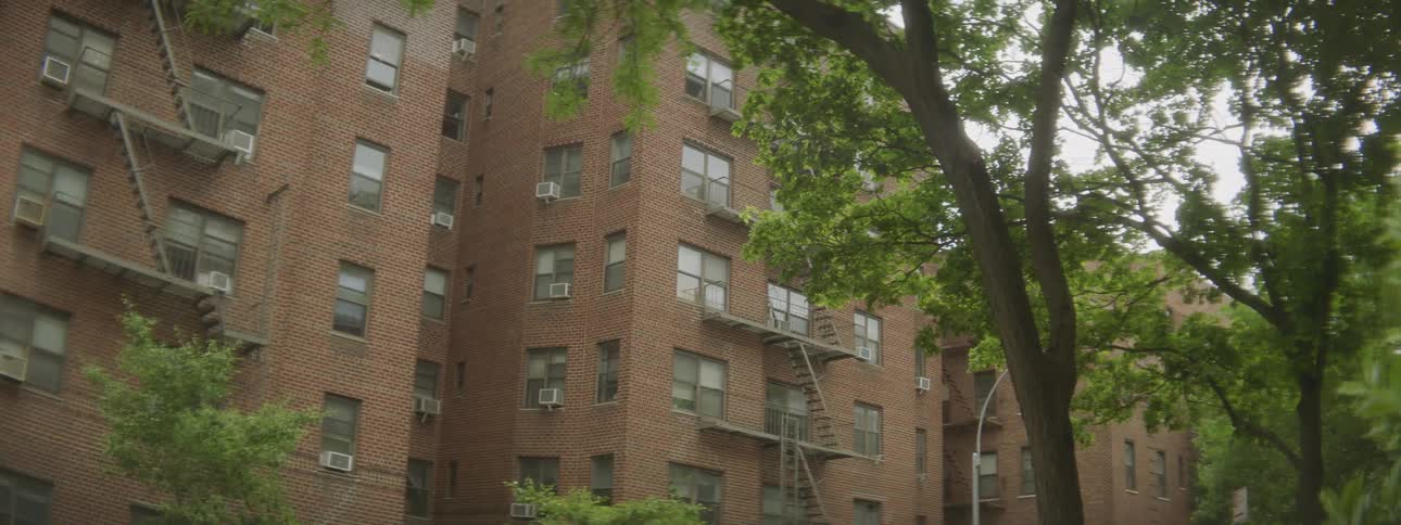 Tall brick buildings with fire escapes sits close together in a neighborhood