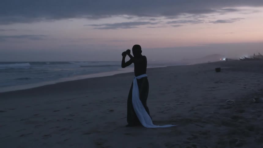 Young teenage boy in traditional costume dancing in the beach near the ocean at sunset