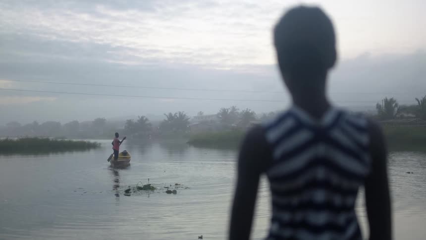 A teenage girl looking at a boy rowing a boat on the mists of a river in the morning