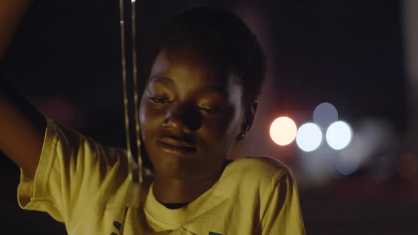 Young teenage girl looking at a necklace hanging from her hand outdoors at night