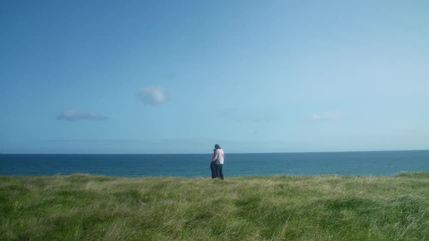 Young couple hugging over the long green grass in front of the ocean at daytime