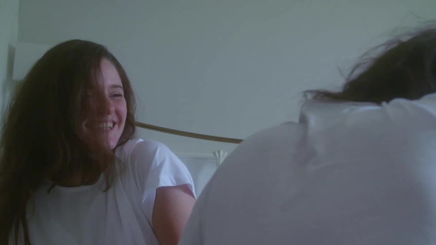 A man and woman couple laugh as they fall in to bed