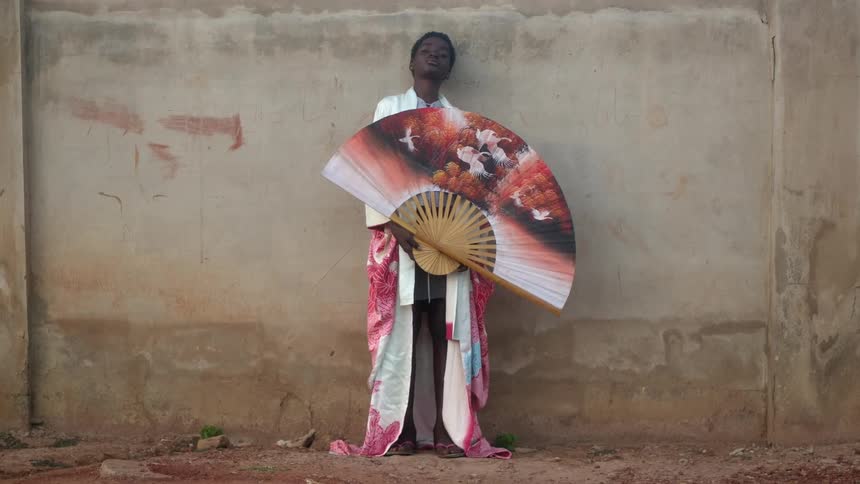 A person standing next to a concrete wall with an ornate fan and robe