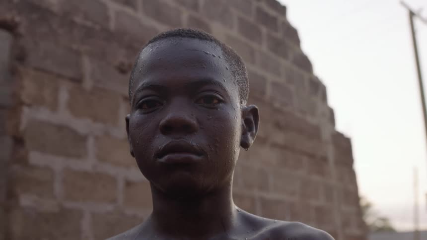 A boy standing and staring by a wall with the sky and clouds in the background