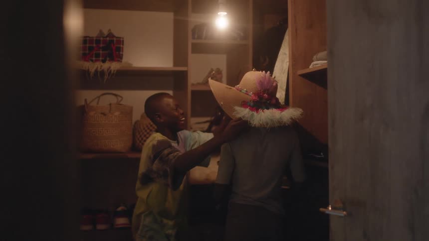 A boy taking a hat from a shelf and putting on the hat on a girl