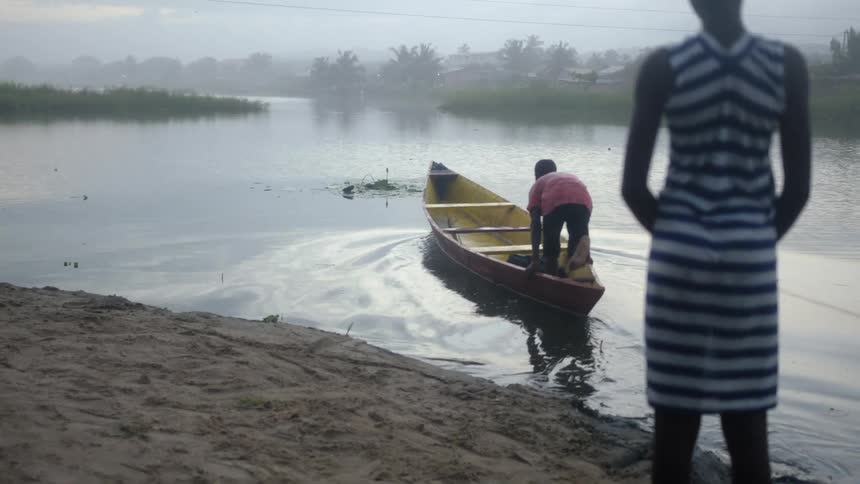 A teenage girl helps a young boy to board a canoe over a river in the morning