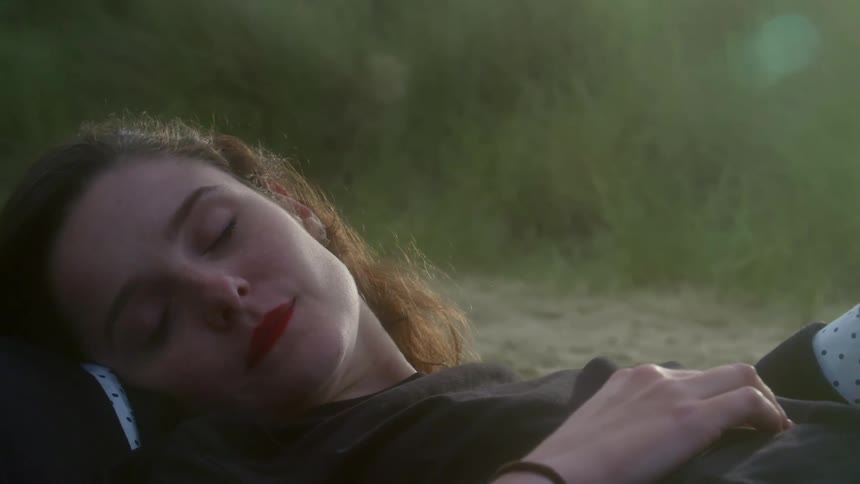 A woman in a relationship and in love is laying in the sand by the beach at sunset.
