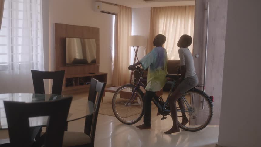 Two boys pedal a two person bicycle into their dining room