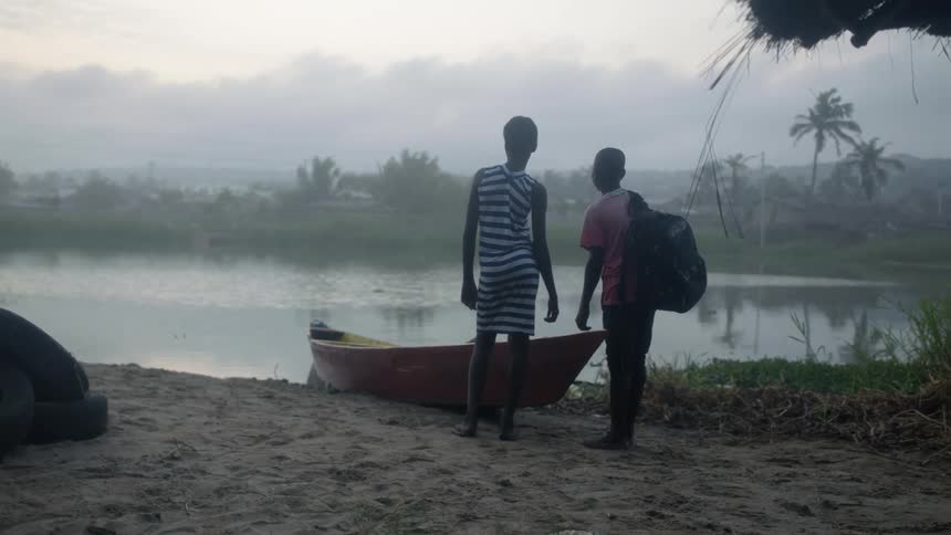 Two boys standing next to a boat at the river