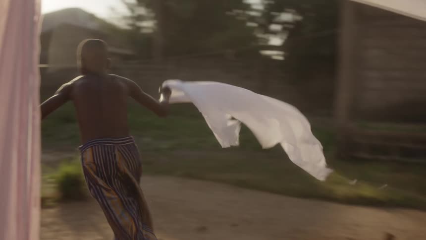A boy decides to steal a white sheet from an outdoor clothes line and takes off running
