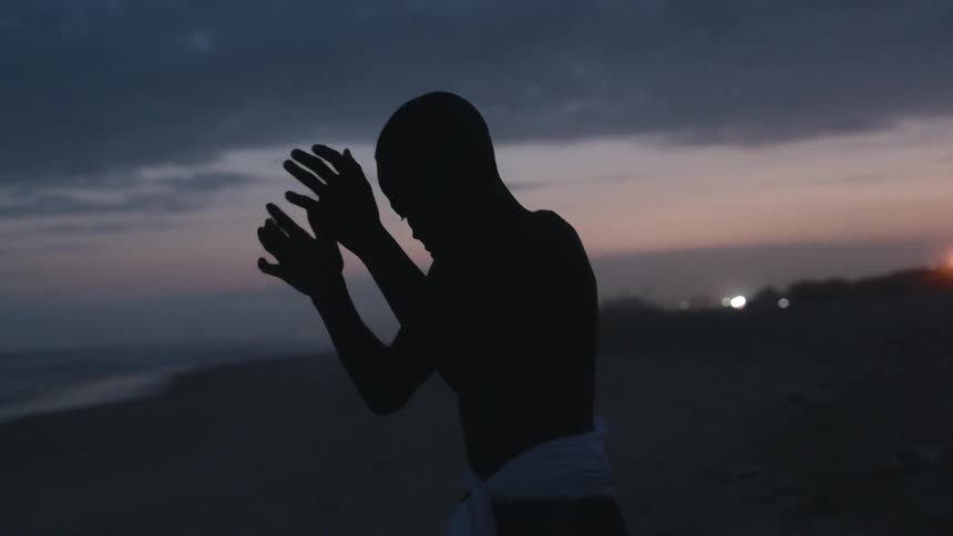 A silhouette of a boy dancing in the beach with the sky and clouds in the background