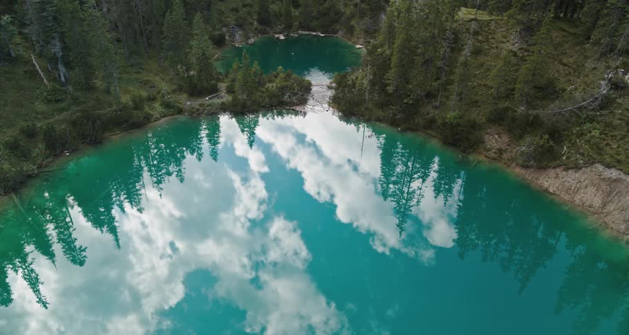 Crater lake with surrounding forest and clouds reflecting in the water