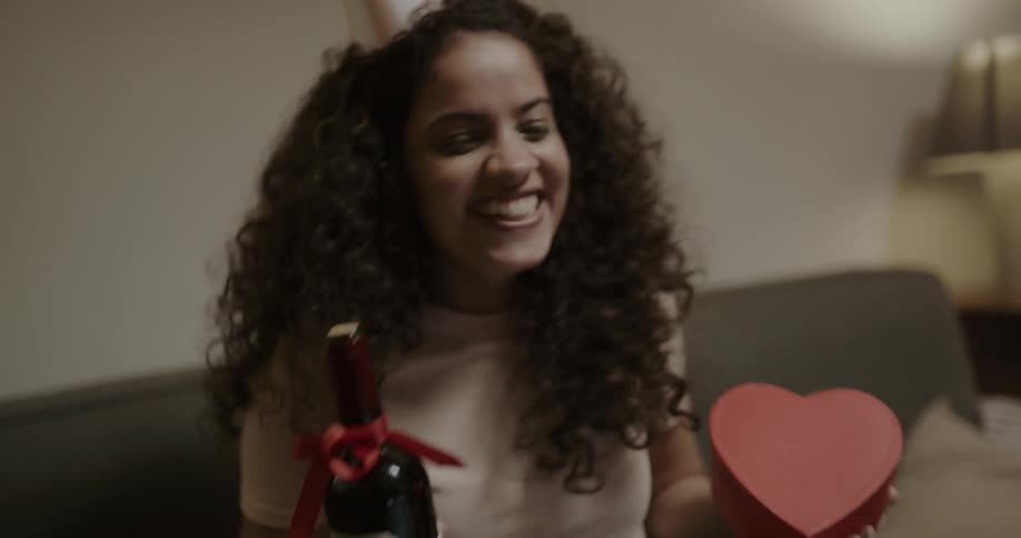 A woman smiling and bouncing on a couch while celebrating a birthday over video chat
