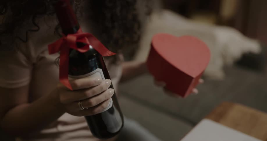 A woman with a party hat smiling while holding wine and a heart shaped box on video chat
