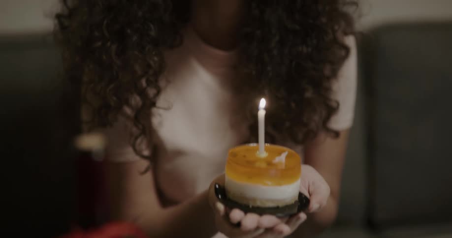 A woman sitting on a couch at home lights a candle on a dessert and then blows it out