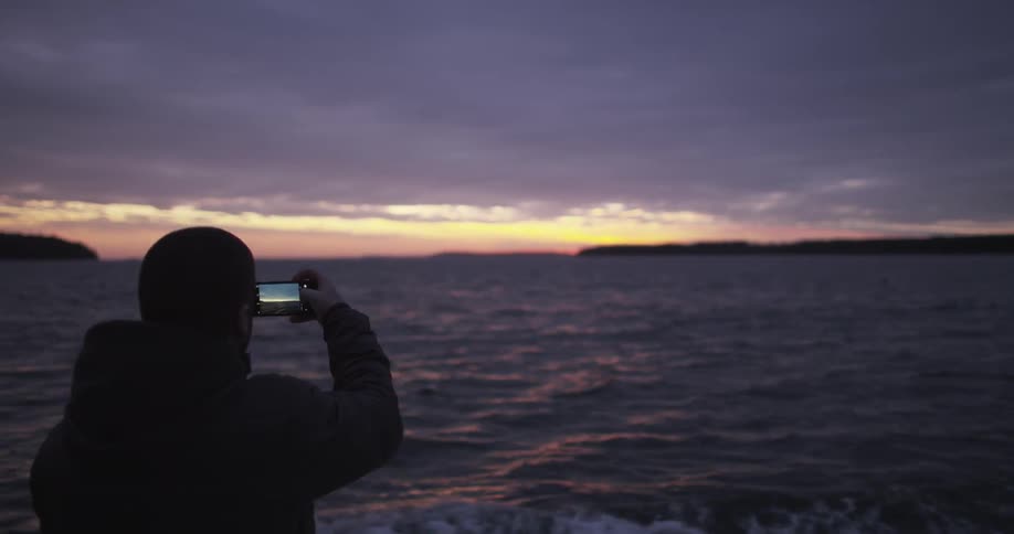 A man uses his phone to take a photo from a moving boat
