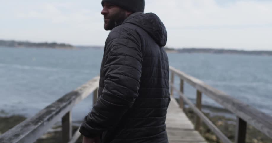 A man standing on a pier zips up his coat