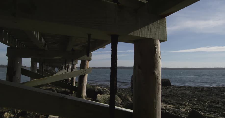 A person walks on the rocks next to the bottom part of a dock