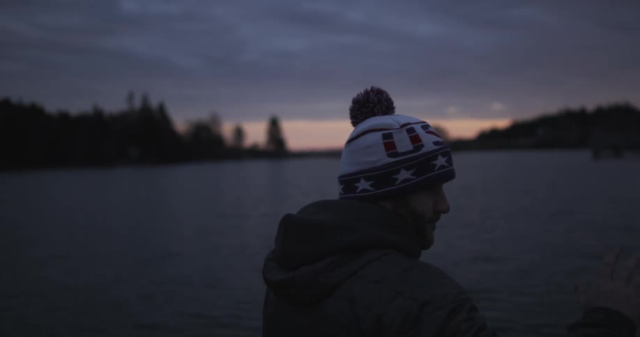 A man is standing by the water at sunset