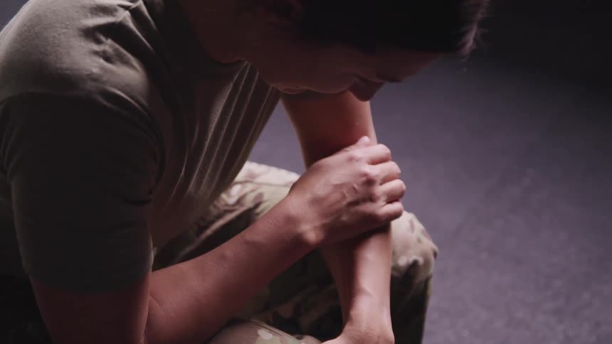 A soldier in camouflage pants sitting hunched over