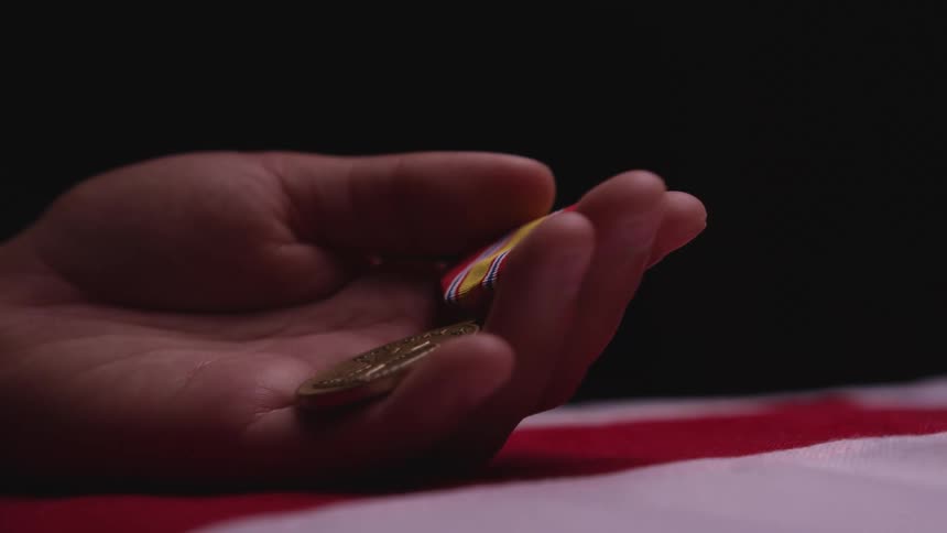 A person holds a gold medal in their palm and caresses the ribbon