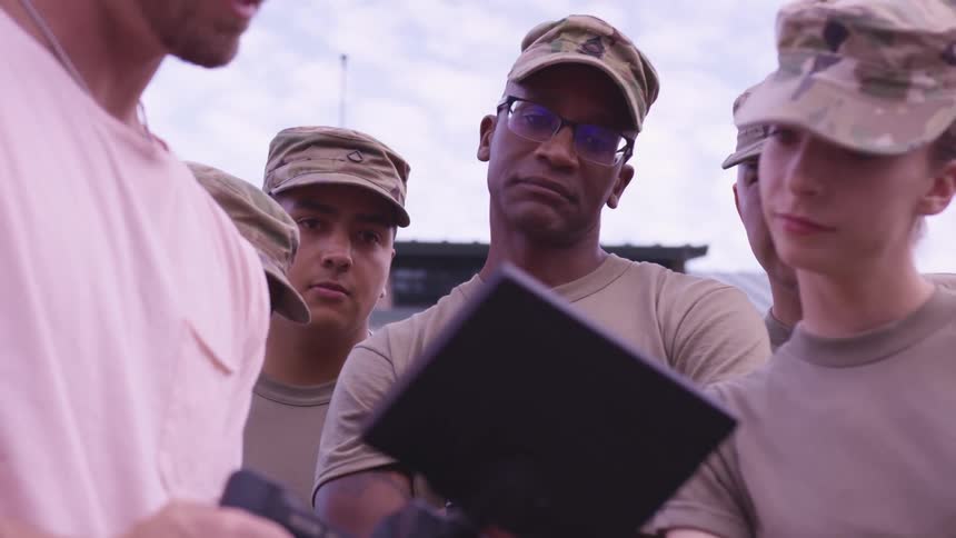 Photographer showing the camera screen to a troop of soldiers standing outdoors