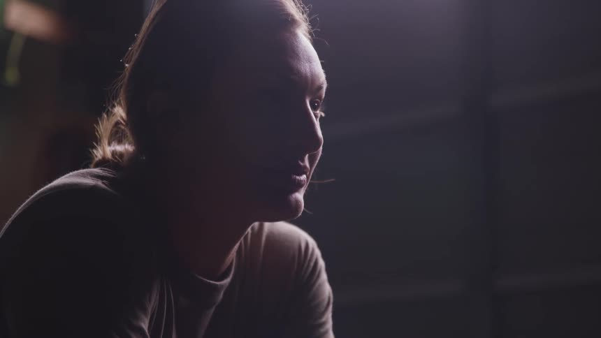 Young woman sitting inside a dimly lit room looking up