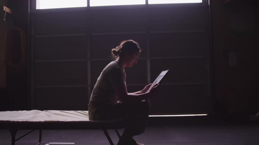 A woman in a military uniform sitting on a bed reading something that is making her sad