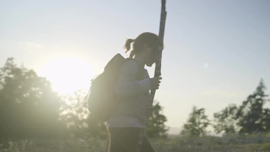 A young girl walks in a forest area carrying a big stick