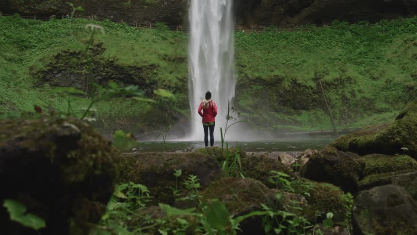 A hiker standing in front of a large gushing waterfall in nature