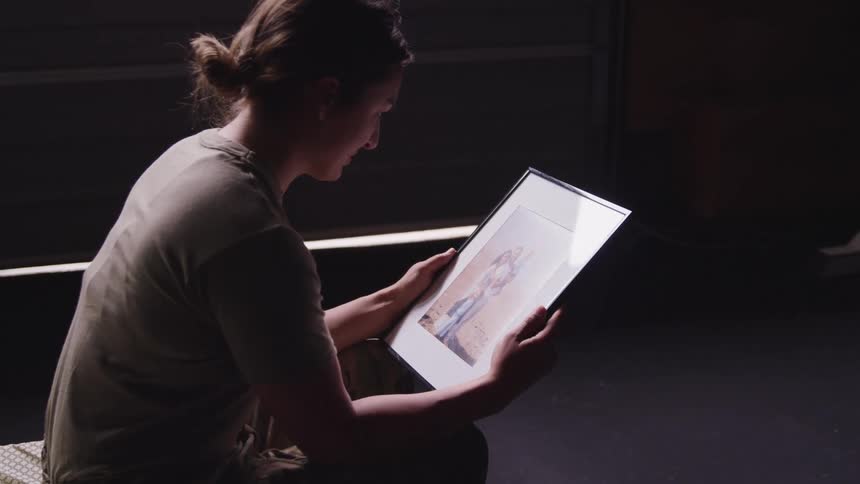 A woman in a military uniform in a room sitting and looking at a picture in a picture frame
