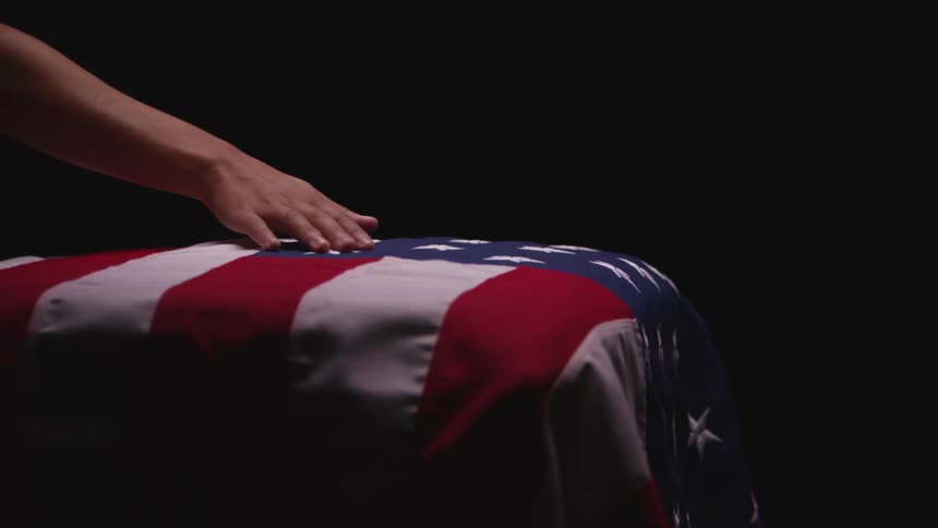 A person in a room touching an american flag draped over a coffin