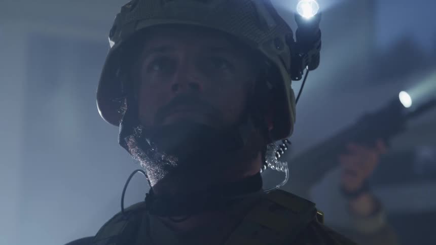 Two men in military uniforms and helmets with flashlights in a room with one of the men pointing a rifle