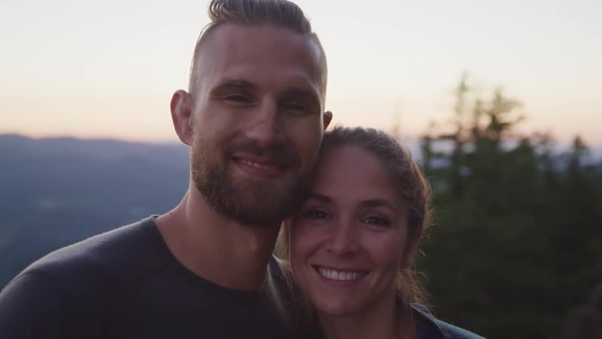 A couple standing close together outdoors smile at the camera