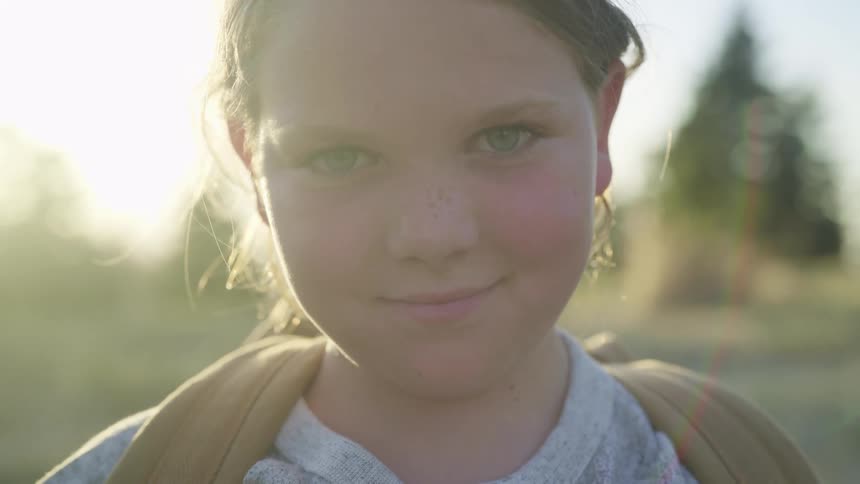 Young girl standing in front of the sun on a field looking at the camera