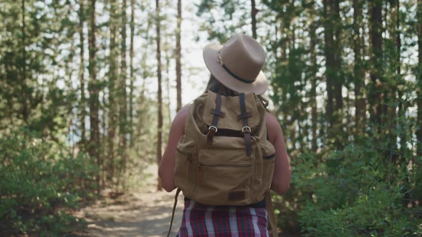 Woman wearing a backpack walking on a dirt trail through the forest at daytime
