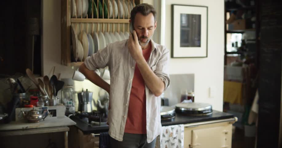 Man speaks on the phone while writing in a notebook in the kitchen