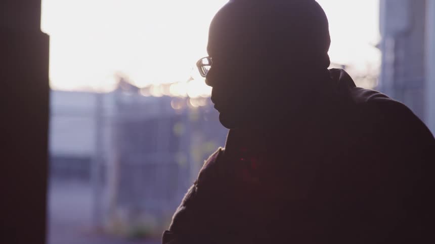 A silhouette of a man with glasses with buildings the sky and clouds in the background