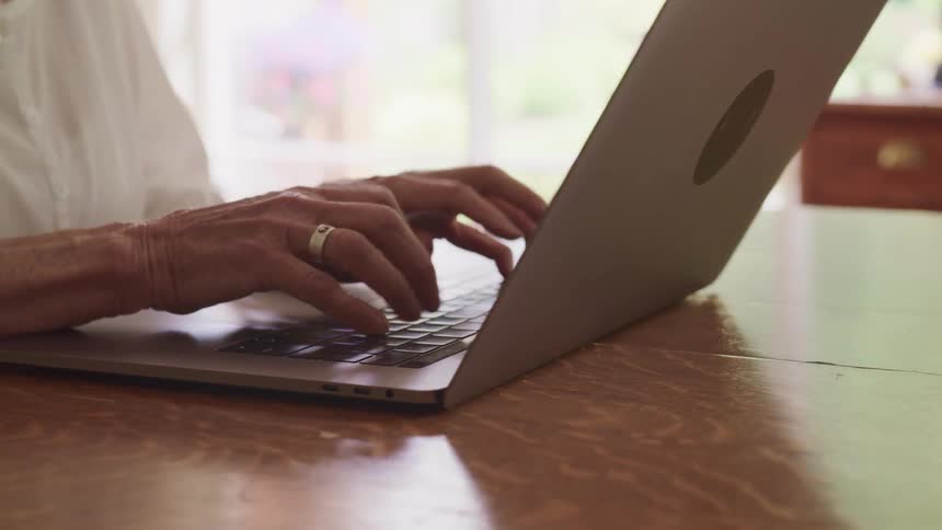 Person wearing a ring on each hand and a white shirt is typing on a laptop keyboard