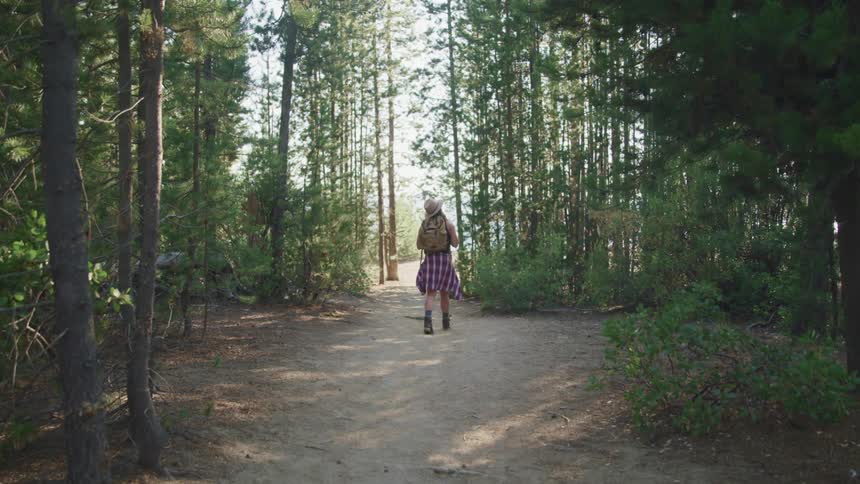 Young woman wearing a backpack walking on a trail through the forest at daytime
