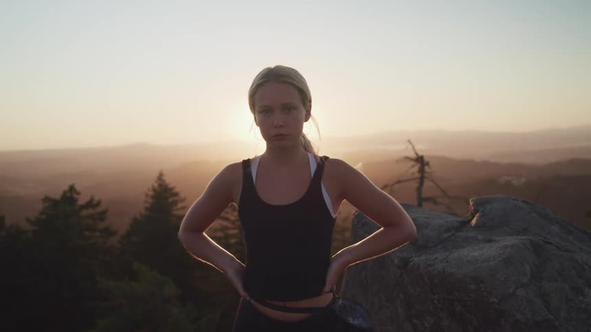A woman poses with her hands on her hips as she stands near the edge of a canyon