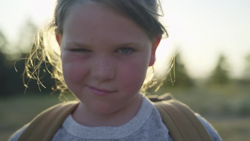 Young girl makes funny gestures looking at the camera while standing outdoors at sunset