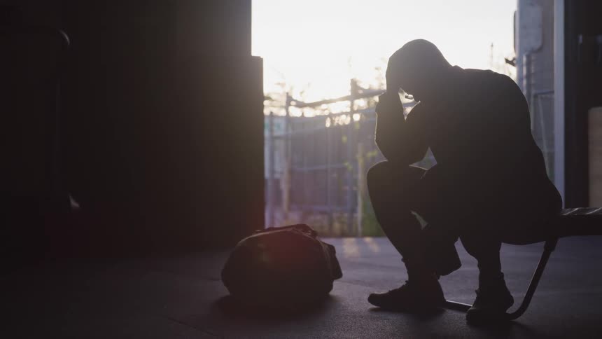 A uniformed soldier sits on the edge of a cot with his head in his hands