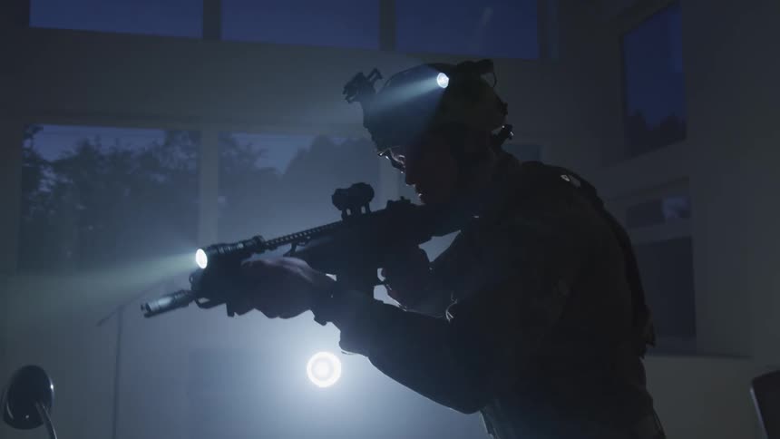 Silhouette of an armored soldier pointing an assault rifle inside a room at night