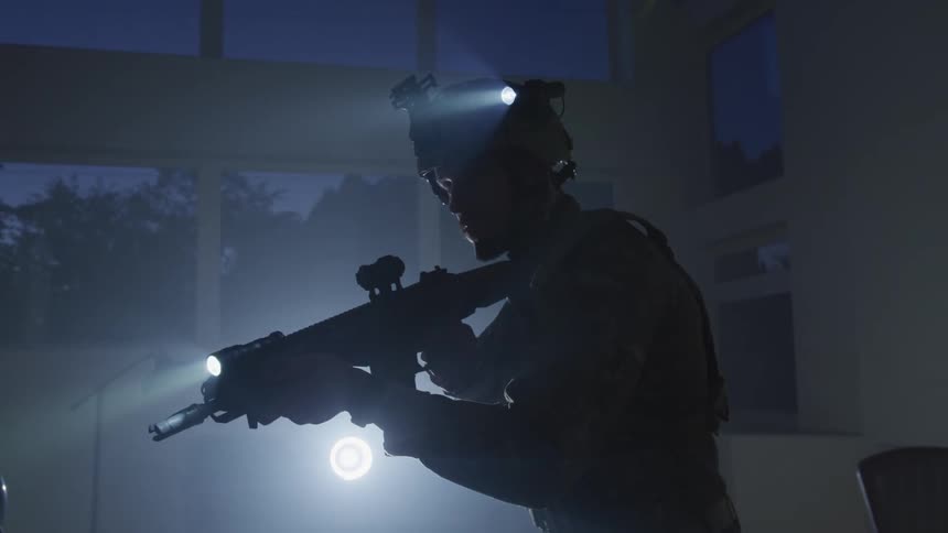 Silhouette of an armored soldier pointing an assault rifle inside a room at night