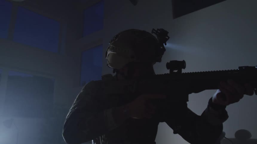 A soldier aims his gun as he scans the dark room he is in