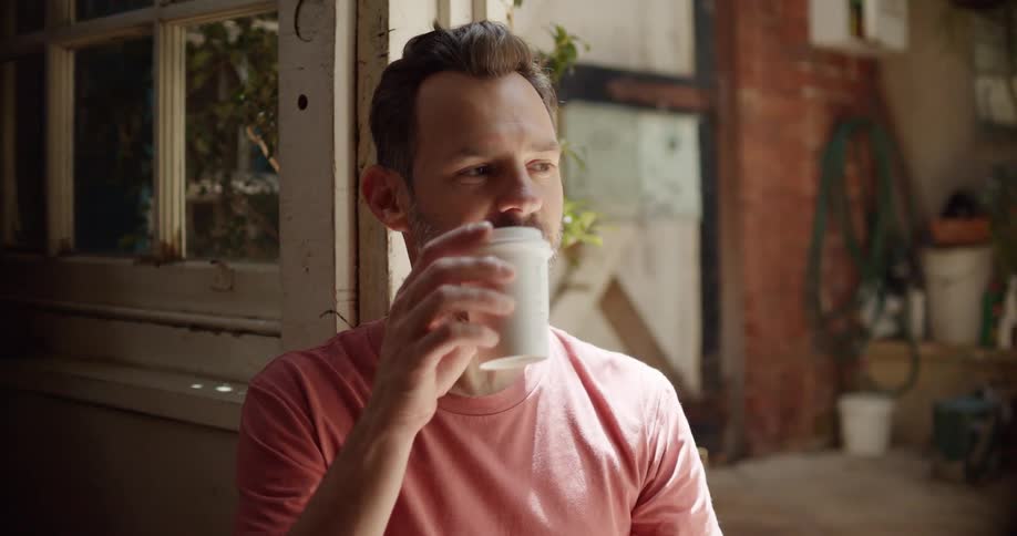 Bearded man drinking from a coffee cup sitting on the doorsteps at home