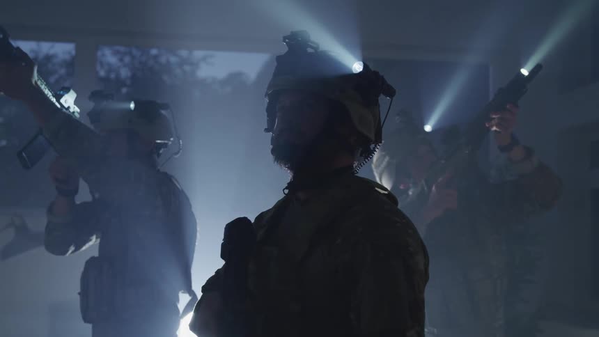 Soldiers stand in a building at night with their weapons raised